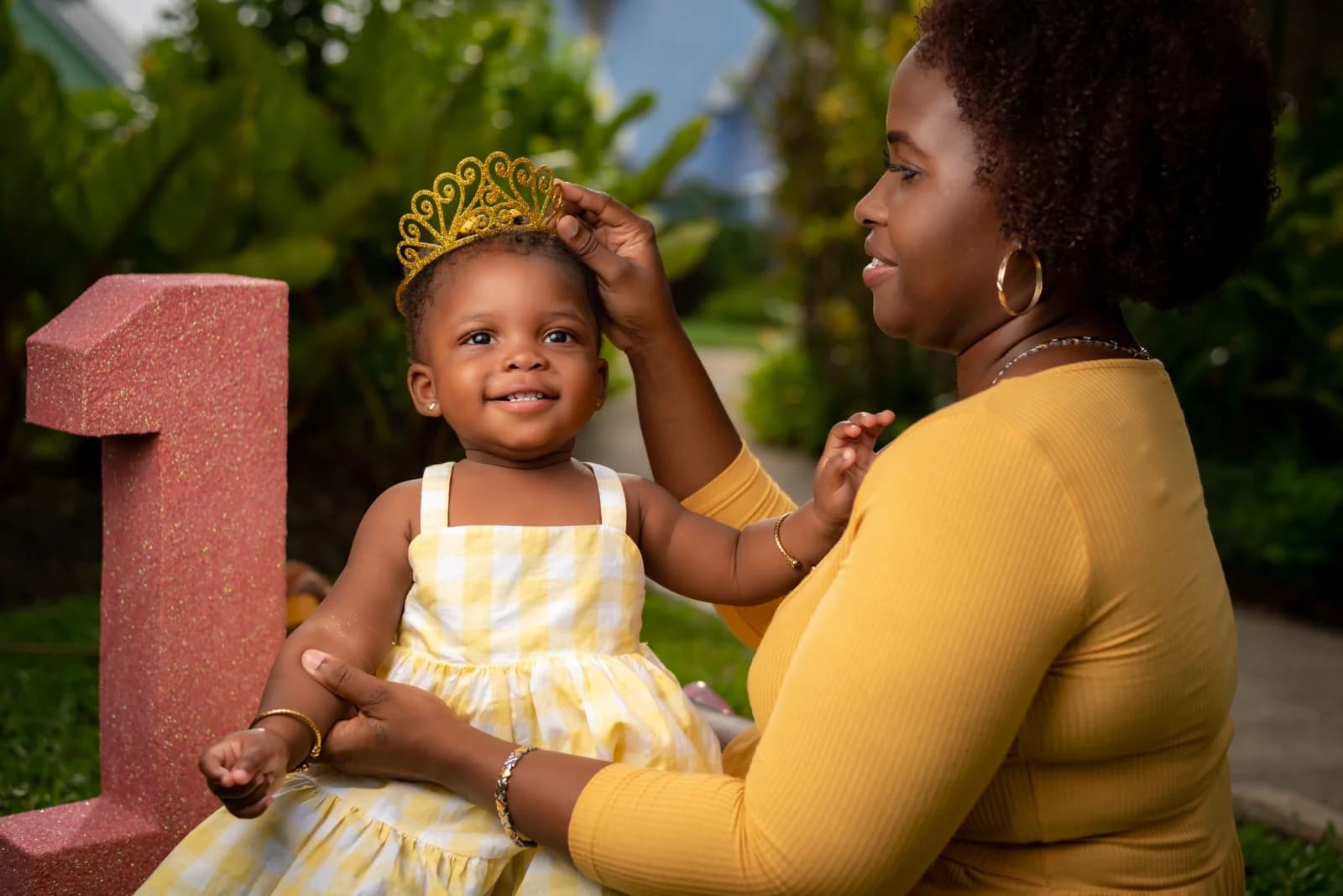 A mother in a yellow top with a smiling child in a yellow and white dress during an outdoor family portrait